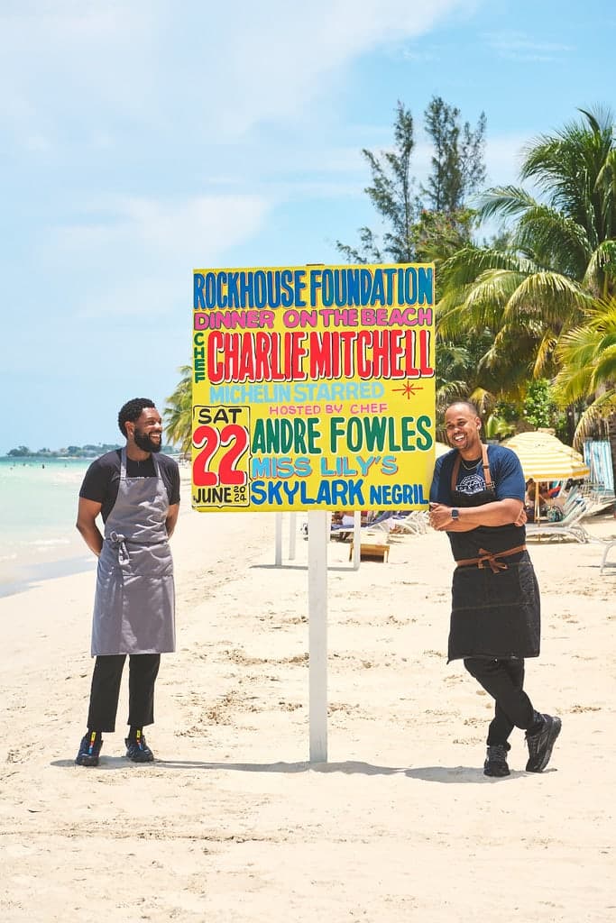 Chefs Charlie Mitchell and Andre Fowles beside the hand painted sign for the Rockhouse Foundation dinner on the beach at Skylark Negril, June 22nd 2024