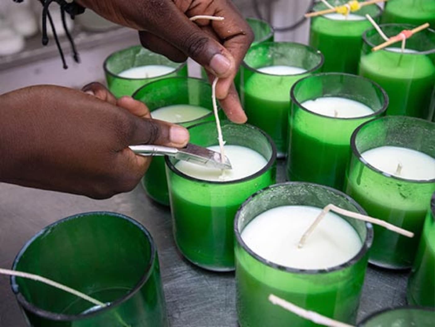 Hands setting wicks into green glass candle jars
