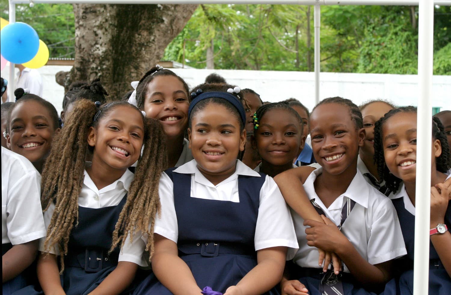 Children in navy and white uniforms smiling together outdoors under a school canopy